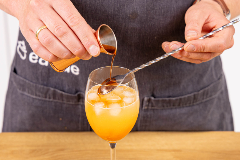 Aperol über die Löffelrückseite ins Glas gießen
