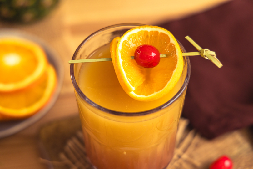 Virgin Sunrise mit Orange und Cocktailkirschen garnieren