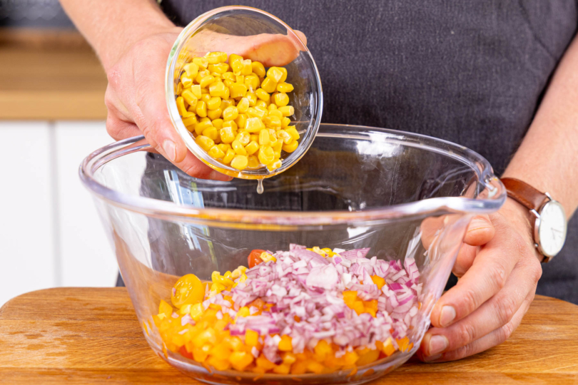 Mais und geschnittene Zwiebel in die Schüssel geben