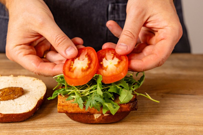 Rucola und Tomatenscheiben auf Leberkäse geben