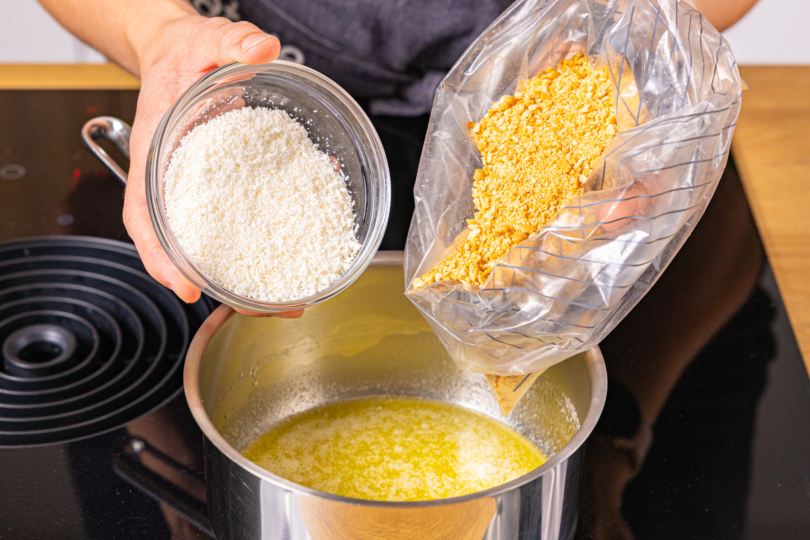 Keksbrösel und Kokosrapel in die flüssige Butter geben