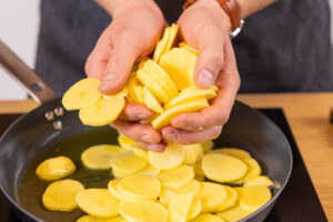 Kartoffelscheiben in die Pfanne geben