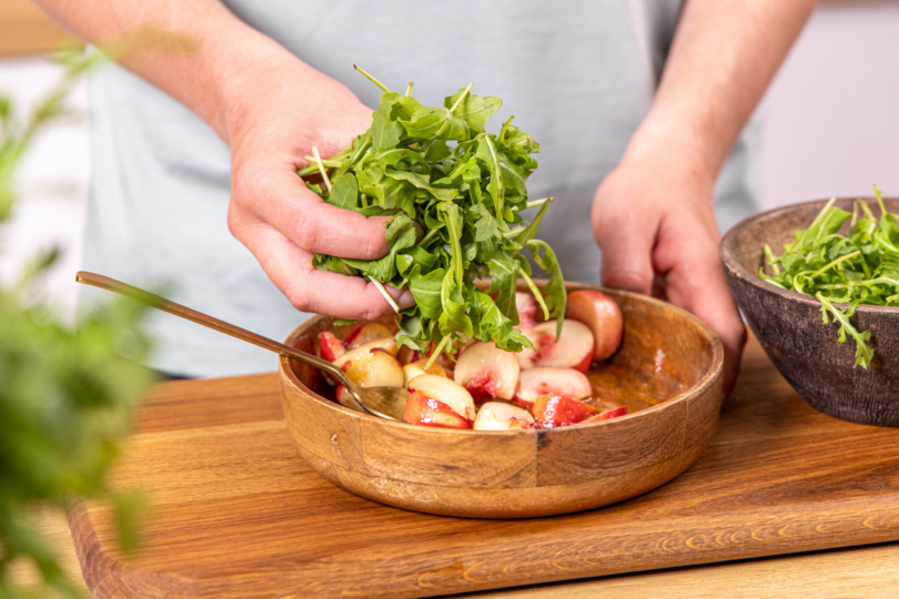 Rucola unter die marinierten Bergpfirsiche heben