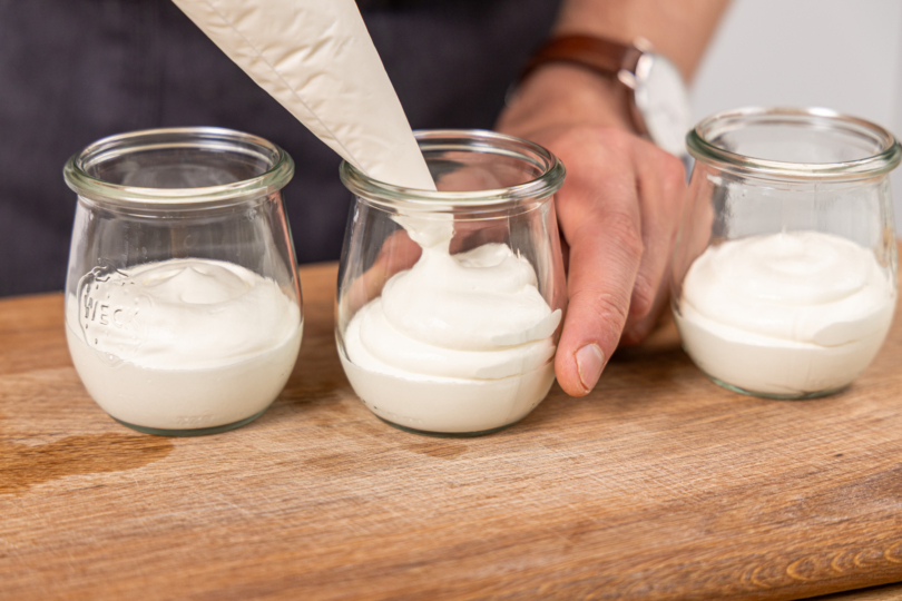 Joghurtcreme mithilfe eines Spritzbeutels in die Gläser füllen