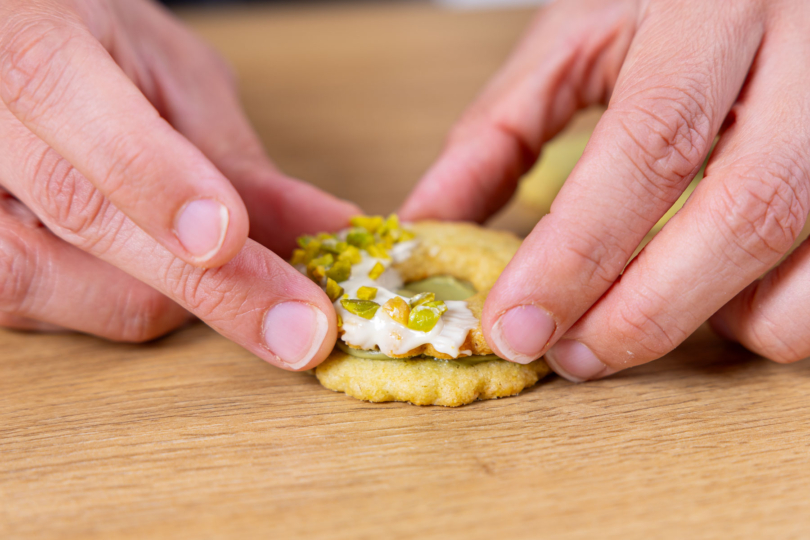 Pistazien-Plätzchen mit der dekorierten oberen Hälfte zusammen setzen