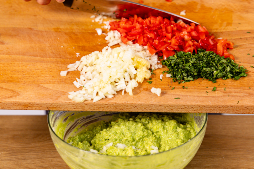 Zwiebel, Tomate und Koriander unter die Avocado mischen