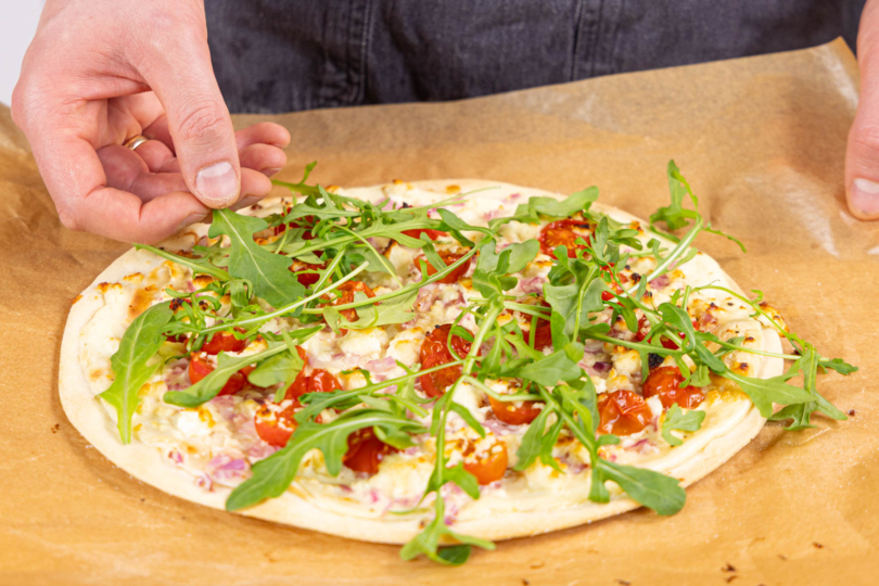 Rucola frisch auf den gebackenen Flammkuchen geben