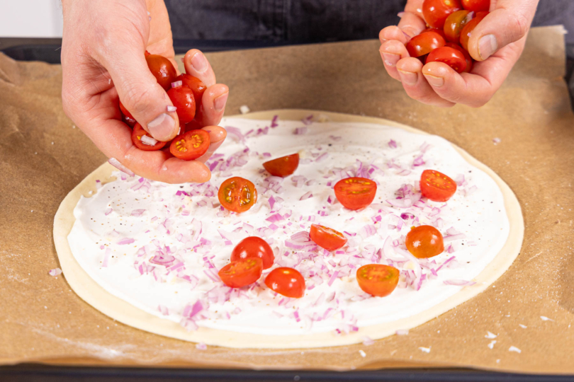 Teig mit Schmand einstreichen und Zwiebel und TOmaten darauf verteilen