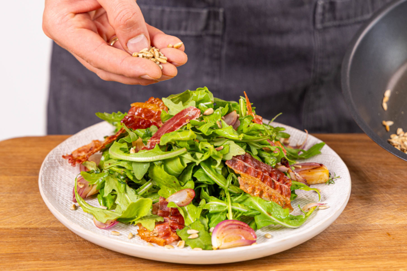 Warmen Rucola-Salat mir Bacon anrichten