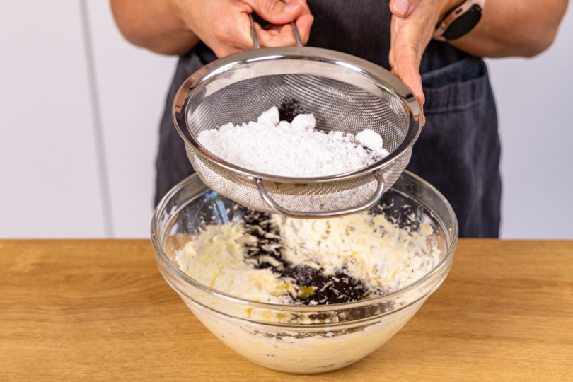 Puderzucker und Kakao zur aufgeschlagenen Butter geben