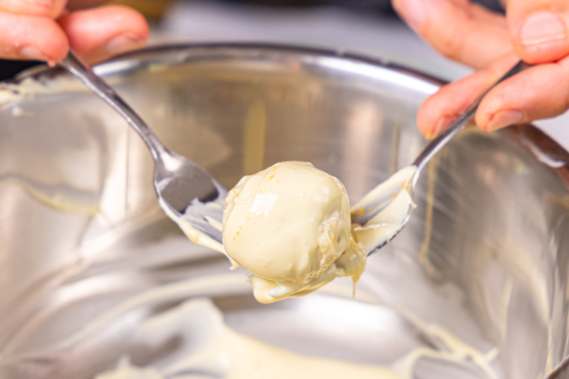 Käsekuchen-Kugeln in weißer Schokolade wälzen