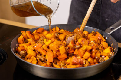 Gemüsebrühe zur Kürbis-Hackfleisch-Pfanne gießen