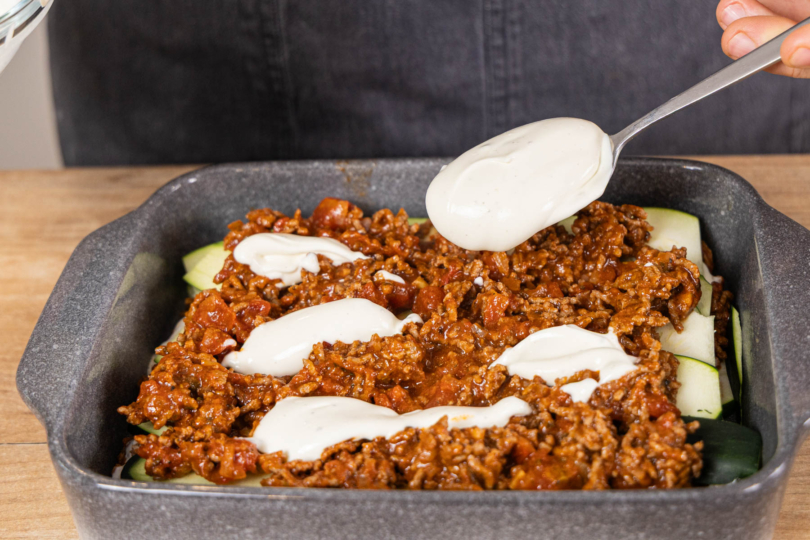 Crème-fraîche-Masse auf die Zucchini-Lasagne mit Hackfleisch geben