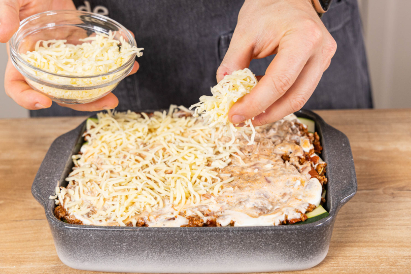 Die Zucchini-Lasagne mit Hackfleisch mit Reibekäse toppen