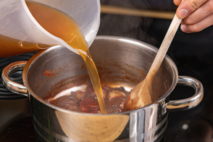 Brühe zur braunen Soße gießen