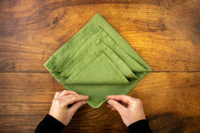 Serviettenspitze in den Händen haltend und nach oben falten.