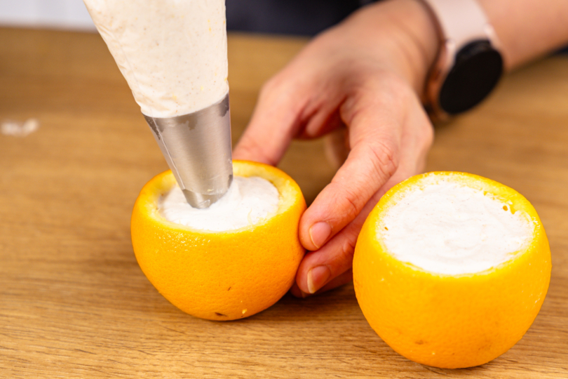 Orange mithilfe eines Spritzbeutels mit der Creme befüllen