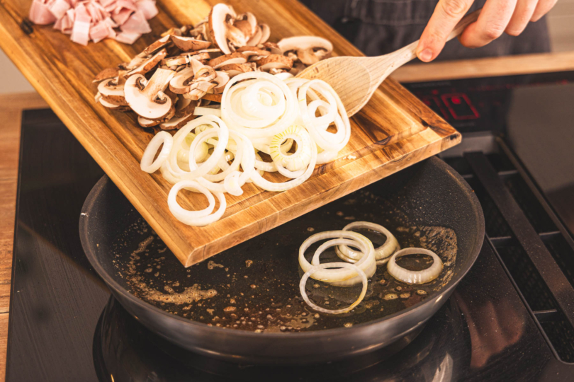 Zwiebelringe und Pilzscheiben in die Pfanne geben