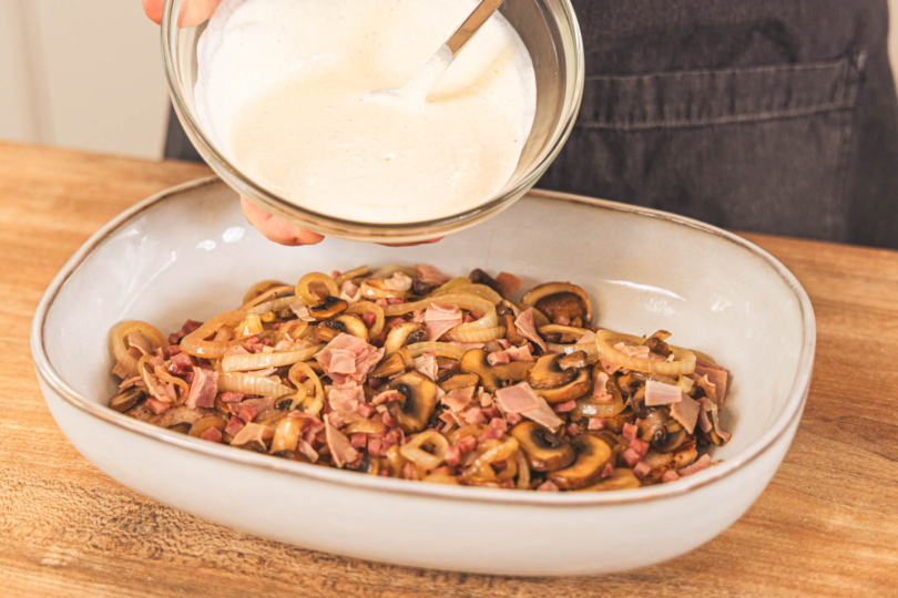 Soße über den Schnitzelauflauf geben