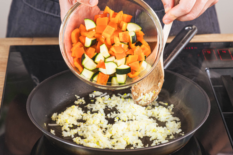 Zucchini und Paprika zu den Zwiebeln in die Pfanne geben