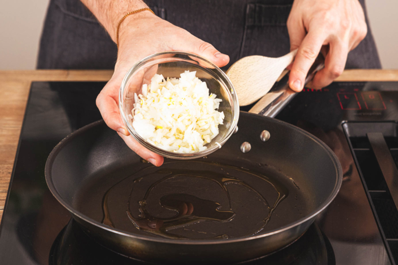 Zwiebel und Knoblauch in die Pfanne geben