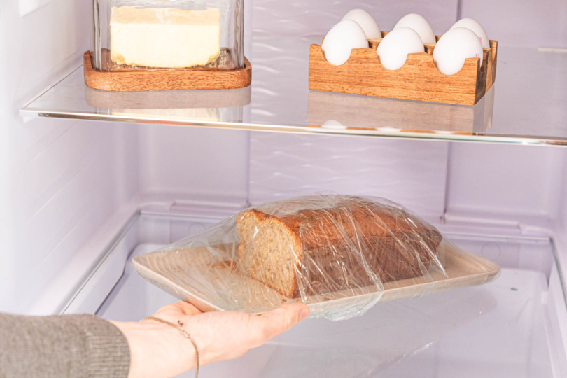 Bananenbrot eingepackt in Frischhaltefolie wird in Kühlschrank gegeben