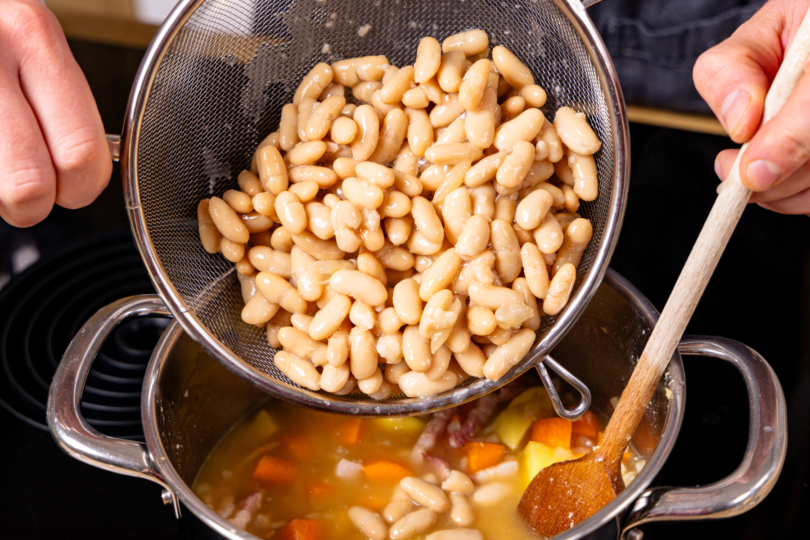 abgetropfte weiße Bohnen zum Eintopf geben