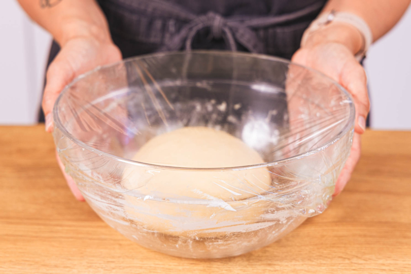 Teigkugel in Schüssel mit Frischhaltefolie abdecken