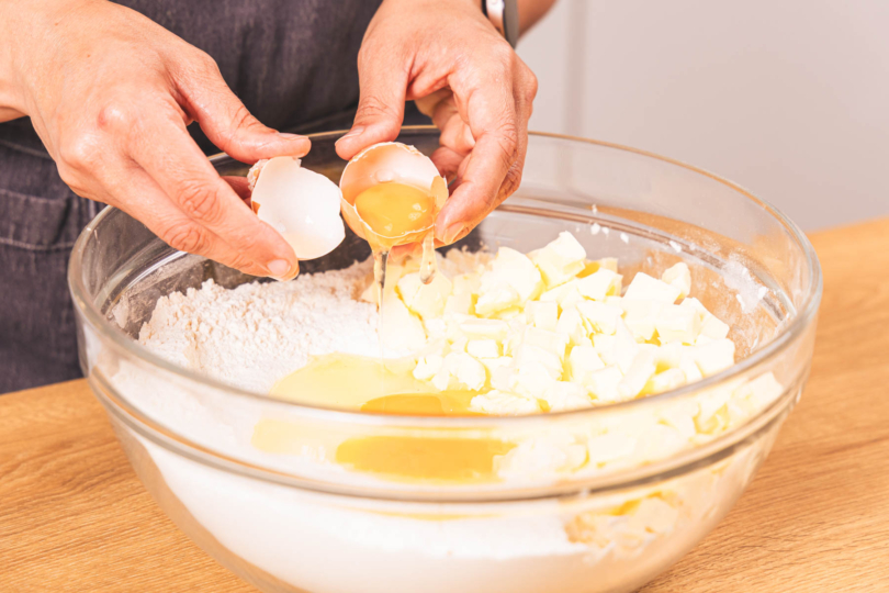 Ei zum Mehl in die Schüssel geben