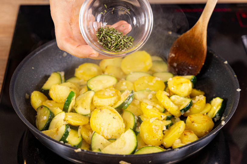 Zucchini-Kartoffel-Pfanne mit Salz, Pfeffer und Kräutern würzen