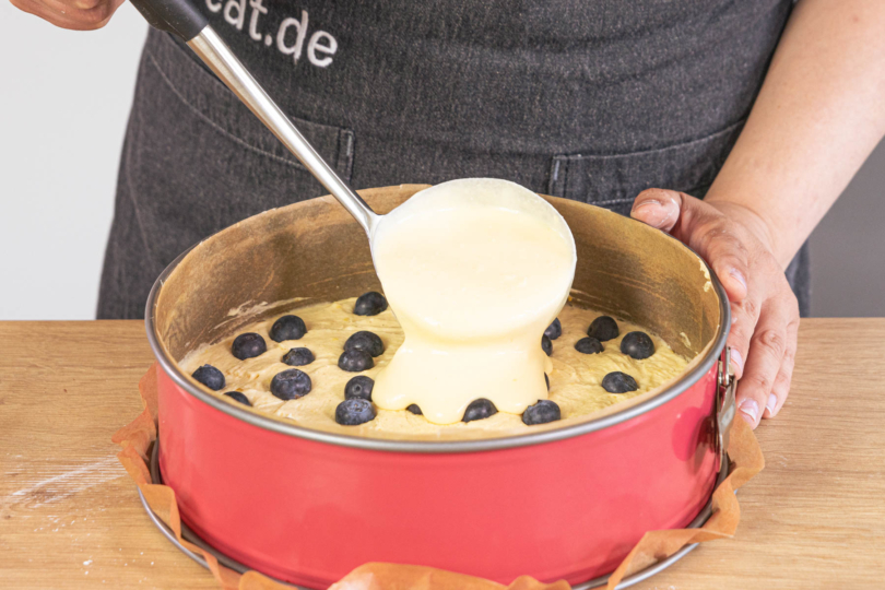 Quarkmasse auf den Rührteig mit Blaubeeren geben