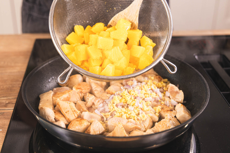 Ananas zum Fleisch in die Pfanne geben