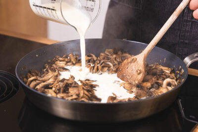 Sahne zu den Champignons gießen