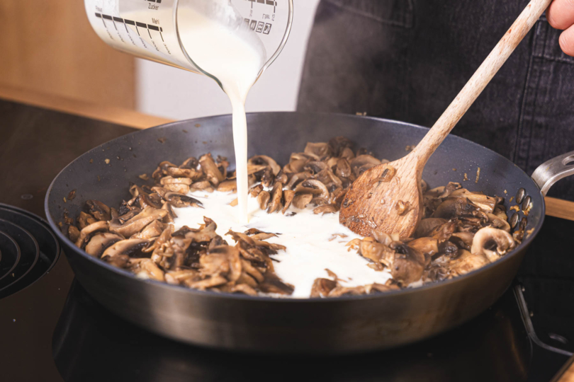 Sahne zu den Champignons gießen