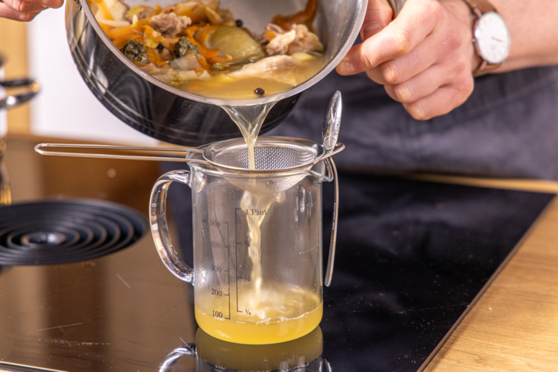 Brühe durch ein Sieb gießen