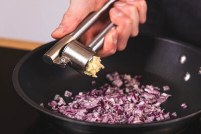 Knoblauch zur Zwiebel in die Pfanne geben