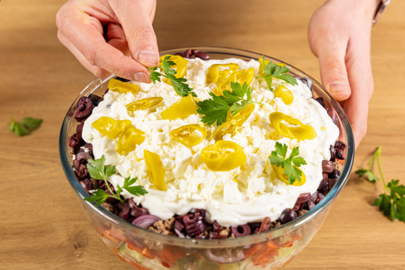 Griechischen Schichtsalat mit Peperoni und Petersilie dekorieren