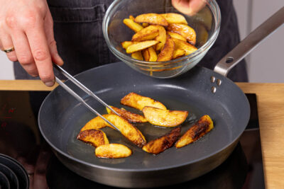 angebratene Kartoffelspalten aus der Pfanne nehmen