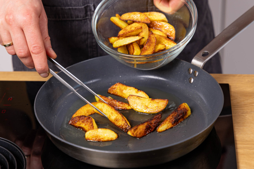 angebratene Kartoffelspalten aus der Pfanne nehmen