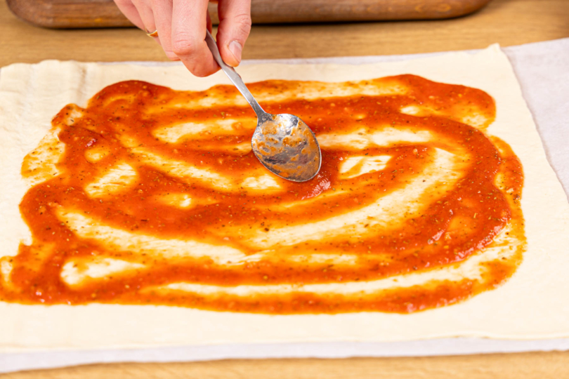 Tomatensauce auf Pizzateig verteilen