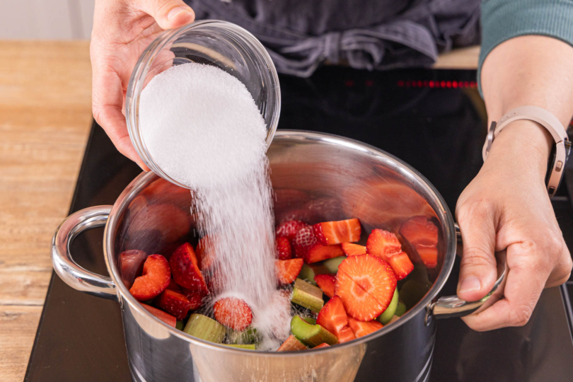 Zucker zu Erdbeeren und Rhabarber in den Topf geben
