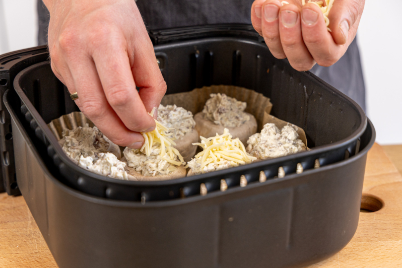 Champignons mit Käse bestreuen und in den Frittierkorb der Heißluftfritteuse geben