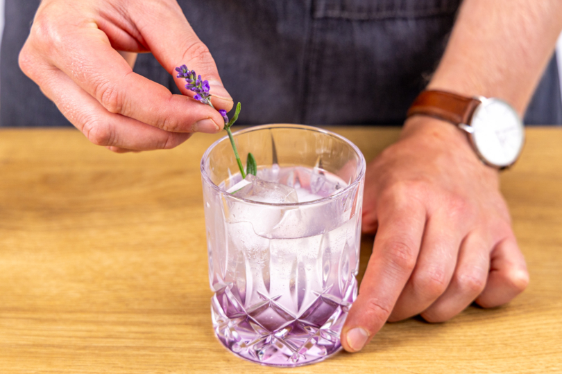 Lavendel Gin Tonic mit einem Lavendelzweig dekorieren