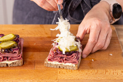 mit Zwiebeln, Gewürzgurken und Krautsalat belegen