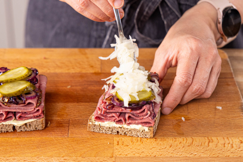 mit Zwiebeln, Gewürzgurken und Krautsalat belegen