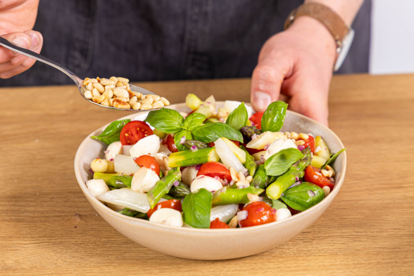 Spargelsalat mit Tomaten und Mozzarella mit Pinienkernen toppen