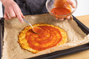 Blumenkohlpizza mit Sauce bestreichen