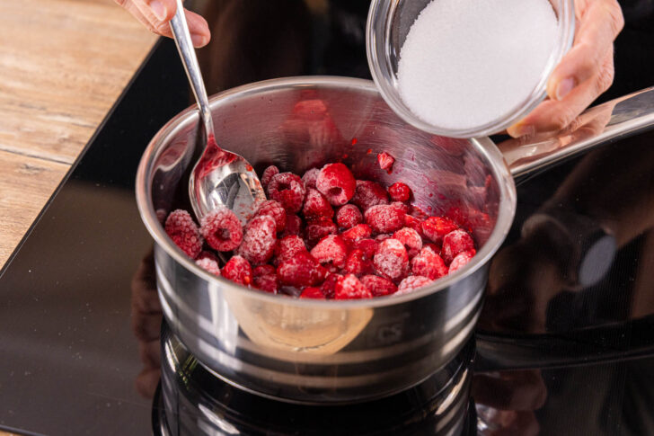 Zucker zu den Himbeeren in den Topf geben