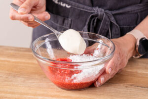 Puderzucker und Schmand zu den zerdrückten Himbeeren geben