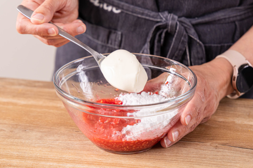 Puderzucker und Schmand zu den zerdrückten Himbeeren geben